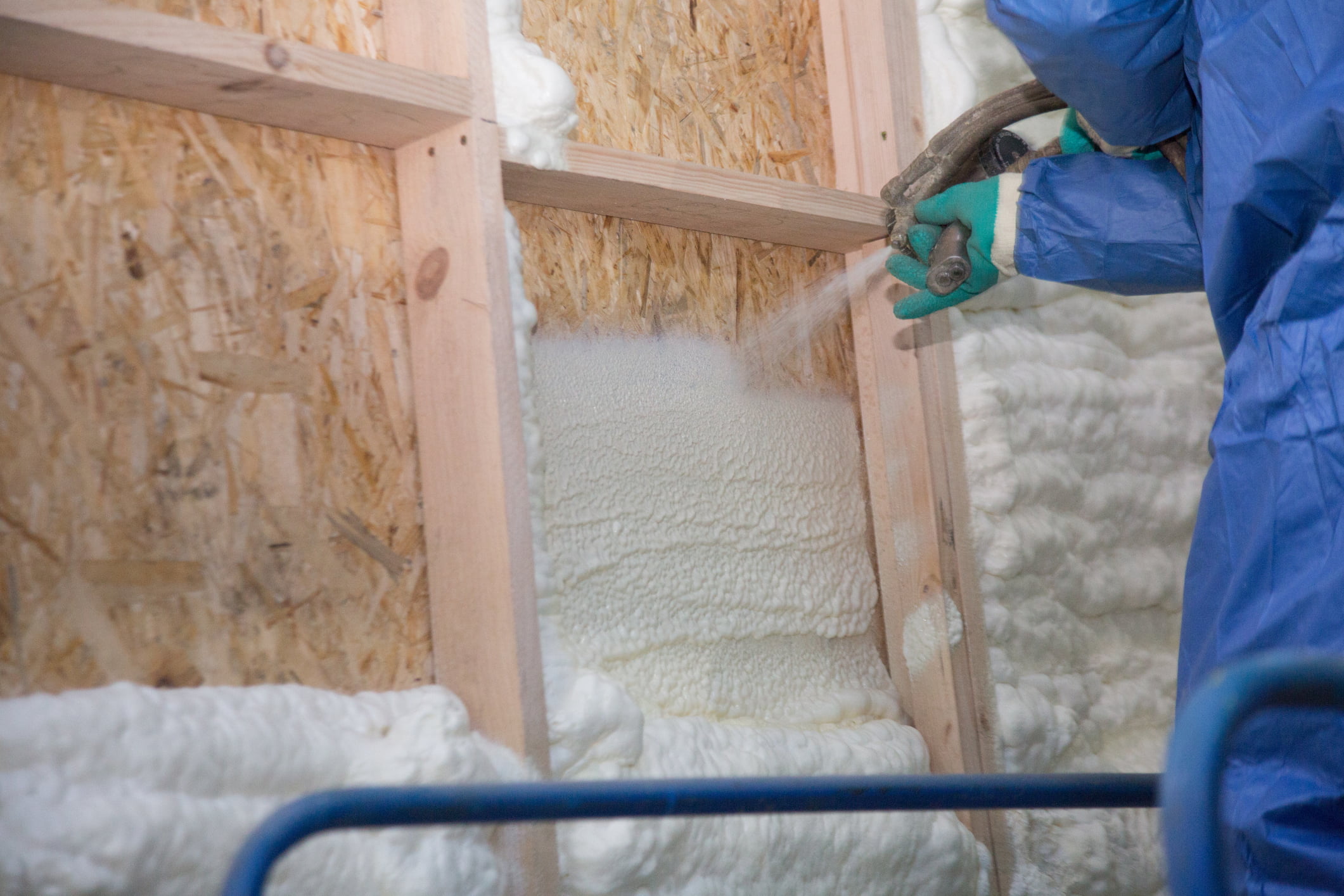 A technician spraying spray foam insulation on to a wall.